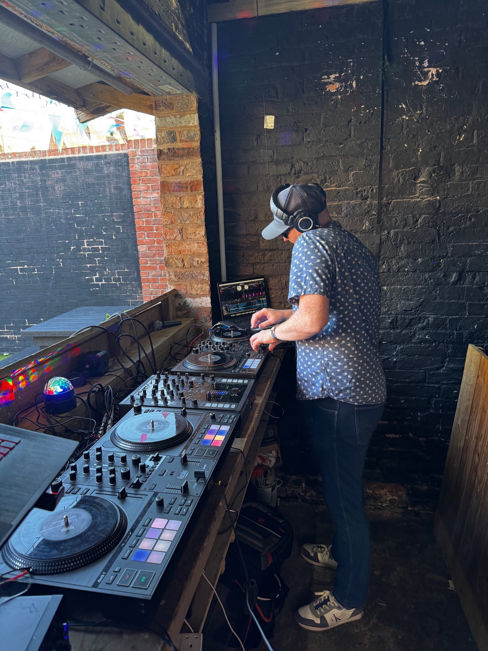 Jamie Hood DJing on turntables in a brick-walled booth